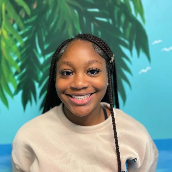 Smiling young girl with braided hair in front of a tropical-themed mural, representing patient satisfaction at Moore Orthodontics.